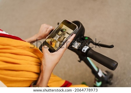 Young indian woman using cellphone while standing with powered scooter outdoors