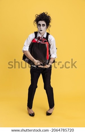 Halloween party shopping. Spooky look. Woman wearing male costue with messy hair and creepy makeup isolated over yellow background. Concept of party, costume, creativity, Halloween. Copy space for ad
