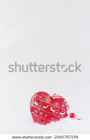 Christmas fun decoration - cute red heart with festive ornament in white sparkling fluffy snow, copy space, vertical.