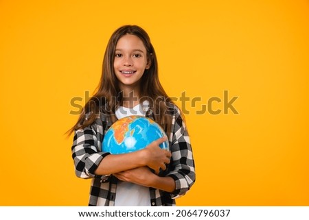 Happy Earth day! Caucasian young teenager schoolgirl pupil student holding hugging globe on geography lesson isolated in yellow background. Royalty-Free Stock Photo #2064796037