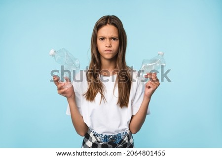 Sad angry disappointed caucasian teenager schoolgirl student pupil eco-activist holding plastic bottles for anti-pollution and environment protection isolated in blue background