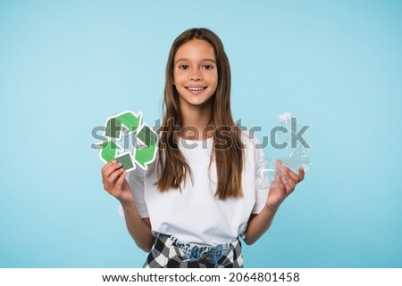 Happy caucasian eco-activist student schoolgirl pupil holding recycling logo sign and plastic bottle for environment protection, sorting garbage isolated in blue background