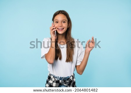 Happy cheerful caucasian schoolgirl teenager pupil student talking on smart phone with friends parents with good connection using mobile application isolated in blue background