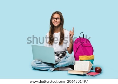 Sitting full-length teenager schoolgirl with laptop computer showing pointing on copy space having idea, surfing webpages on Internet,social media,e-learning remotely isolated in blue background Royalty-Free Stock Photo #2064801497