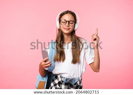 Happy caucasian schoolgirl teenager listening to the music going back to school pointing showing copy space isolated in pink background Royalty-Free Stock Photo #2064802715