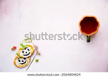 Halloween still life with pumpkin cup with tea and homemade cookies in shape of sweet pumpkins. Bright pink aesthetic autumn holiday or trick or treat concept. Copy space. Home cooking and coziness.