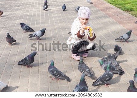 a girl in the spring in the park photographs pigeons with a children's camera. She's wearing a white jacket and hat