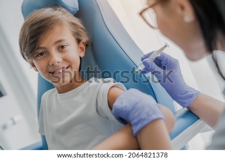 Vaccination concept. Female caucasian doctor nurse vaccinating with a syringe cute smiling little teenage boy in clinic hospital against infectious disease