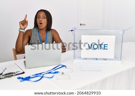 Young african american woman working at political election sitting by ballot pointing finger up with successful idea. exited and happy. number one. 