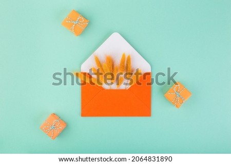 Orange envelope and dry flowers, lagurus, with copy space, on blue table with small gifts. Season gift-giving concept