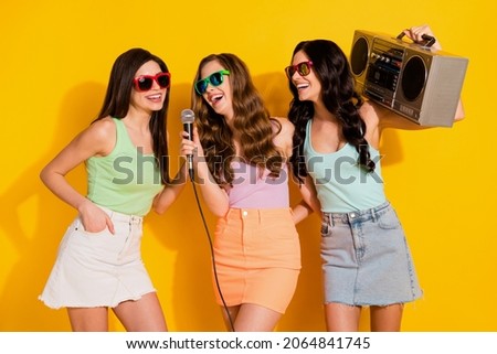 Photo of young happy excited girls hold boombox on shoulder sing karaoke isolated on yellow color background