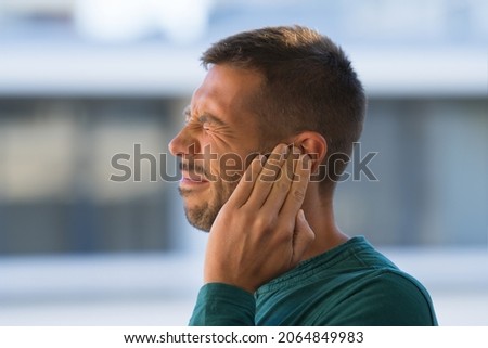Otitis or tinnitus. Man touching his ear because of strong earache or ear pain.  Royalty-Free Stock Photo #2064849983