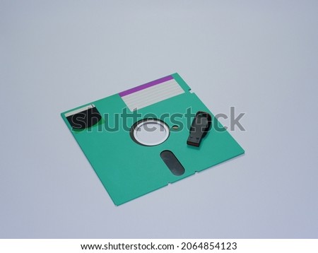 5.25-inch diskette as a data storage area with small capacity compared to large capacity and more modern USB flash drive. Green floppy disk and black USB flash drive on white background isolated.