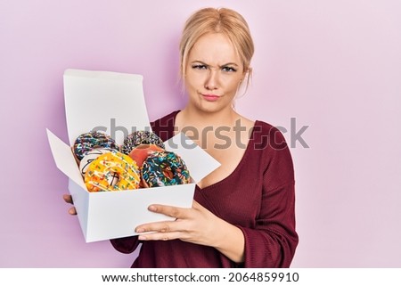 Young blonde woman holding tasty colorful doughnuts skeptic and nervous, frowning upset because of problem. negative person. 