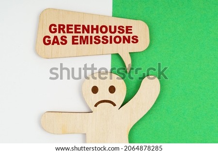 Environmental concept. On a green and white background, a sad wooden figure of a man and a plate with the inscription - greenhouse gas emissions