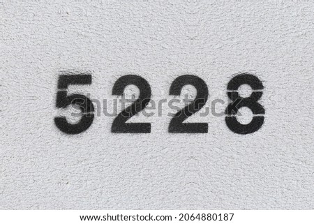 Black Number 5228 on the white wall. Spray paint. Number five thousand two hundred and twenty eight.