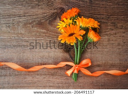 Bouquet from flowers of calendula with orange satin ribbon on wooden background