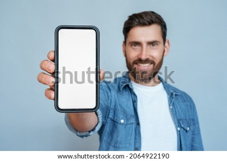 Satisfied confident smiling caucasian man showing mobile phone blank white screen mockup to camera standing isolated on blue studio copy space. Closeup smartphone in male hand. Advertisement concept Royalty-Free Stock Photo #2064922190