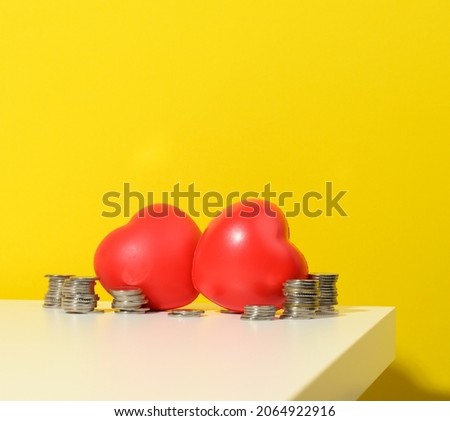 stack of coins and red heart on white table