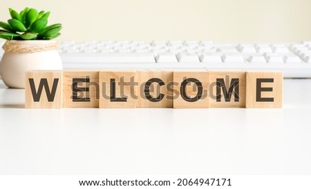 welcome word made with wooden blocks. front view concepts, green plant in a flower vase and white keyboard on background