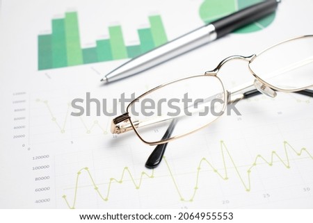 Business composition with laptop glasses and pen over financial and statistics sheets with analysis graphs on a workdesk