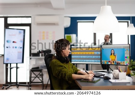 Creative photographer using digital retouching software, wearing headphones editing photos for client. Stylish retoucher, graphic editor working in creative multimedia workplace