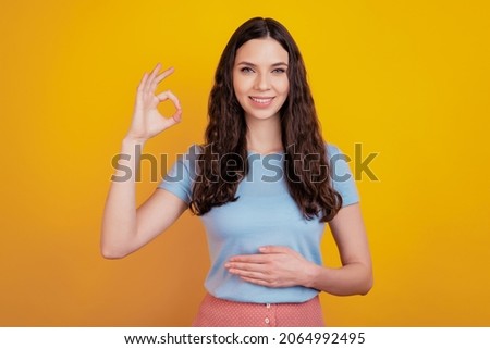 Photo of cheerful cute pretty nice girlfriend showing you ok sign hand on belly isolated over yellow color background Royalty-Free Stock Photo #2064992495