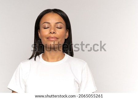 Calm peaceful african american woman with closed eyes and relaxed smile breathing deeply focused on positine thinking and meditating. Young female relaxing or recovering after stress or panic attack Royalty-Free Stock Photo #2065055261