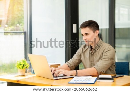 Businessman holding pen pointing to the graph to analyze marketing plan with calculator and laptop on wooden table in office Finance and Accounting Concepts	