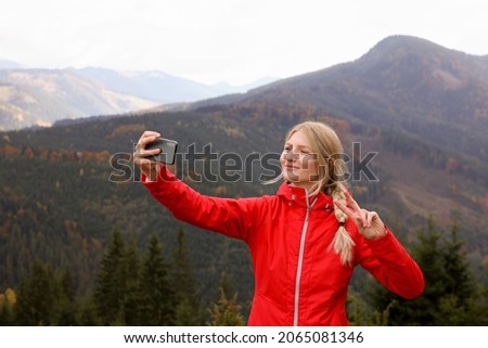 Happy young woman taking selfie with phone in mountains