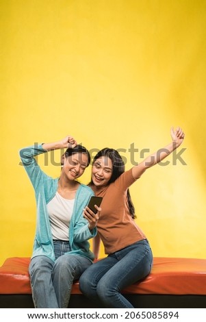 excited two beautiful asian girl with hands up while looking smartphone