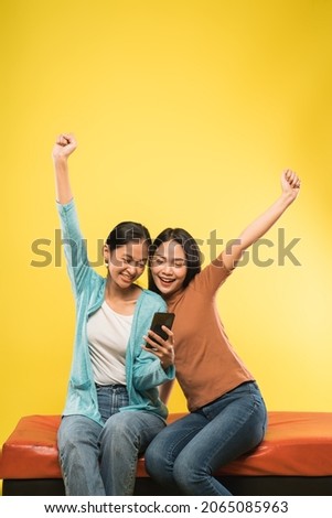 two asian woman happy with hands up when surprised looking a mobile phone screen