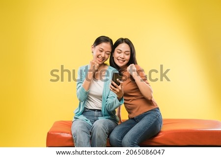 two young woman happy with hands clenched when looking a mobile phone screen
