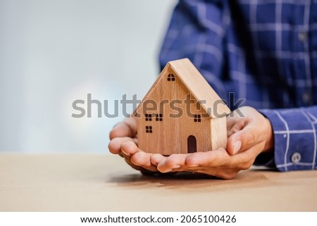 Businessman choosing mini wood house model from model and row of coin money on wood table, selective focus, Planning to buy property.