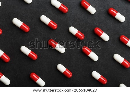 A pattern of red and white pill capsules on a black background background. Pharmaceuticals, medicine, vitamins