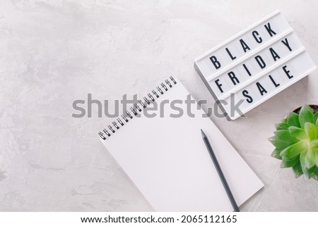 Black friday sale word written on lightbox, plant, empty notebook with place for text on light background. Flat lay, top view. Selective focus