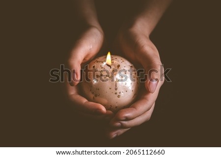 Hands holding Christmas candle on black, symbol of faith and religion