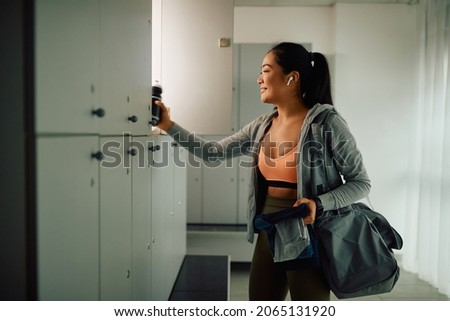 Happy Asian athletic woman taking her stuff from a locker after finishing sports training in a gym. Royalty-Free Stock Photo #2065131920