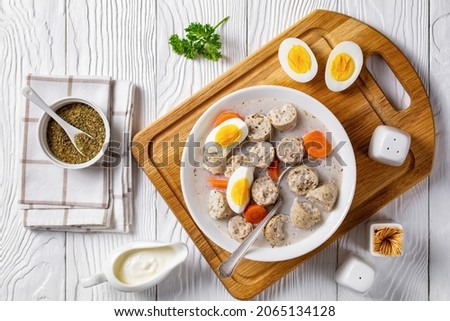 Zurek polish fermented rye cereal soup with traditional polish kielbasa or sausage with marjoram, hard-boiled eggs served on a white bowl with a spoon, on a white wooden background, top view