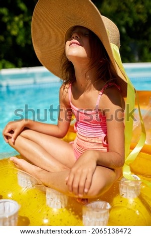 Portrait of little girl in hat relaxing in swimming pool, swims on inflatable yellow mattress and has fun in water on family vacation, tropical holiday resort.