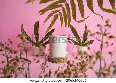 Minimalist concept displaying products. mug on wood, dried flowers and dried leaves on pink background
