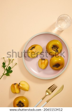 Top view of pink dish of persimmon , pork , knife , water glass in light pink background for food advertising