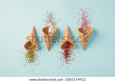 Top view photo of three staggered ice cream cones with christmas decorations explosion of red silver pink and gold sequins on isolated pastel blue background