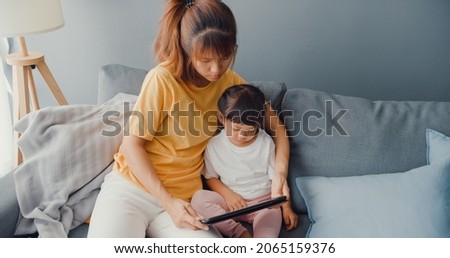 Happy cheerful Asia family mom and cute kid using digital tablet interest cartoon and watch movie having fun relax on couch in living room at house. Spending time together, Quarantine for coronavirus.