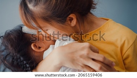Happy cheerful Asia family mom holding sick toddler girl in arms and attach antipyretic gel and kiss on baby forehead in living room at house. Medical care insurance, treatment and healthcare concept.