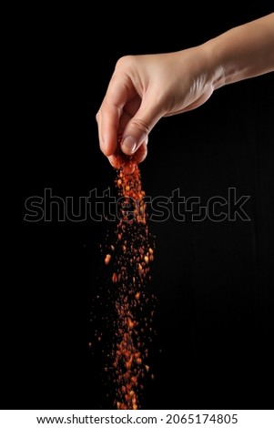 Hand sprinkling cayenne pepper isolated on black background Royalty-Free Stock Photo #2065174805