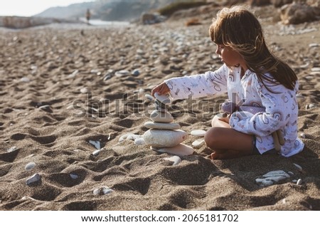 balance, girl sitting on the beach and makes a tower of stones, vacations, relax