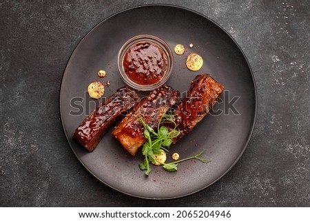 Grilled ribs with sauce and herbs on a black plate Royalty-Free Stock Photo #2065204946