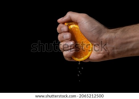 Hand squeezes juice from an orange on a black background. Fresh and juicy orange Royalty-Free Stock Photo #2065212500
