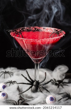 Top view of red halloween cocktail with smoke on table with spider web, black background, vertical